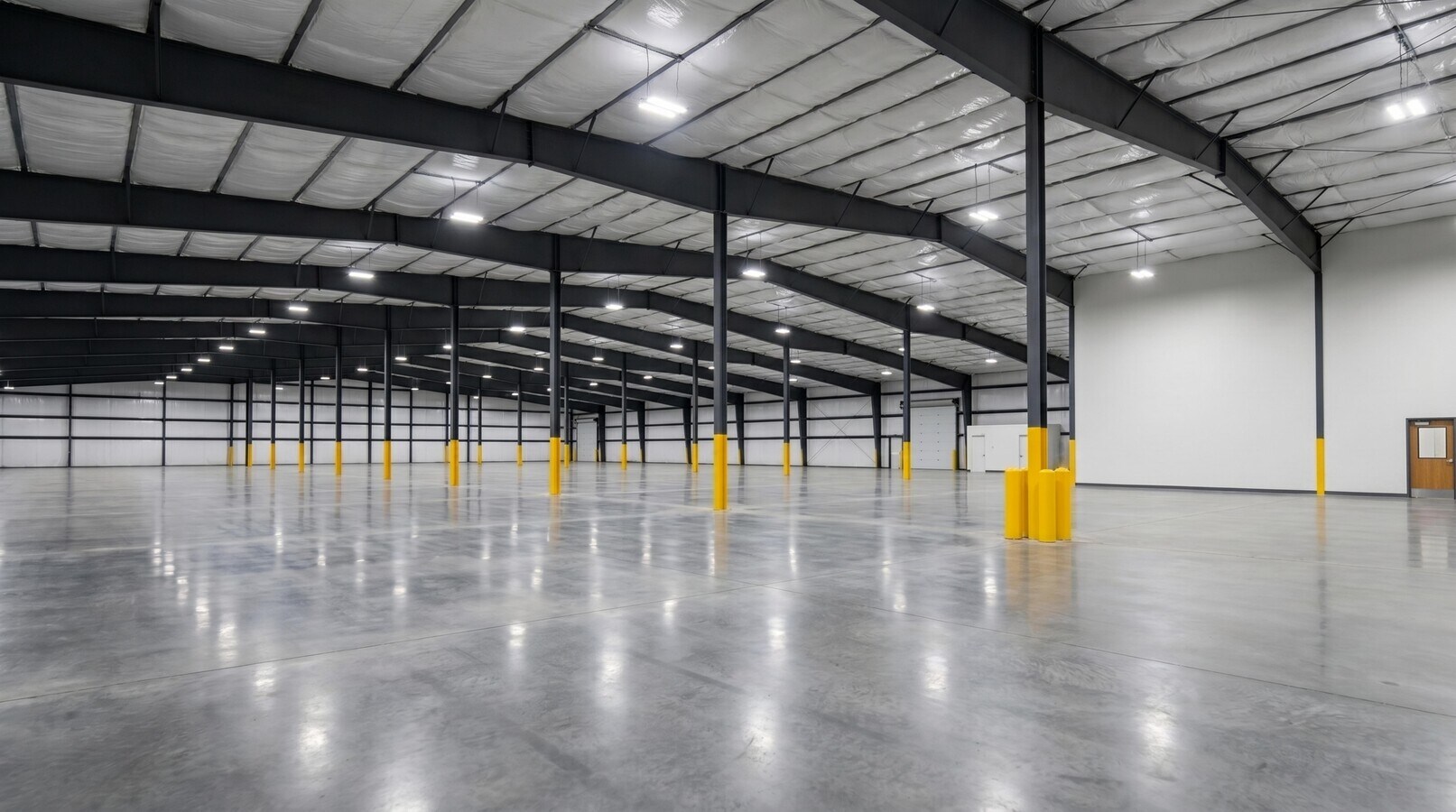 Warehouse interior with polished concrete slab, black steel frame, new LED fixtures and yellow-guarded columns.